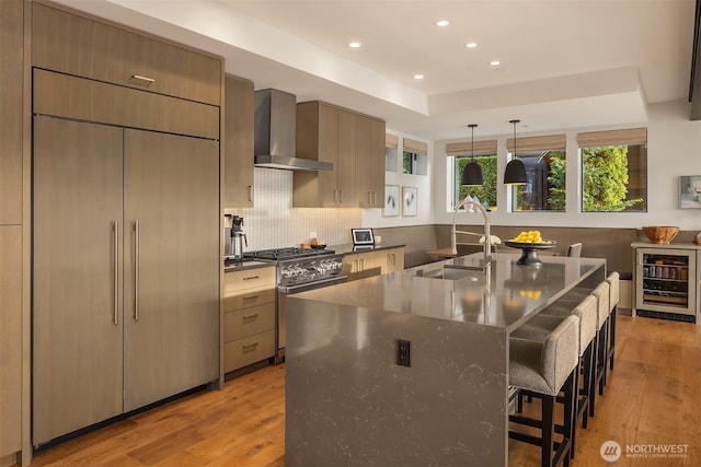kitchen featuring stainless steel gas range, a sink, wall chimney range hood, built in fridge, and wine cooler