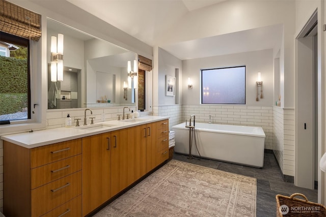 full bathroom with a sink, a freestanding bath, tile walls, and a wainscoted wall