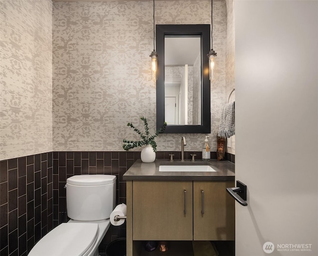 half bath featuring toilet, vanity, and wallpapered walls