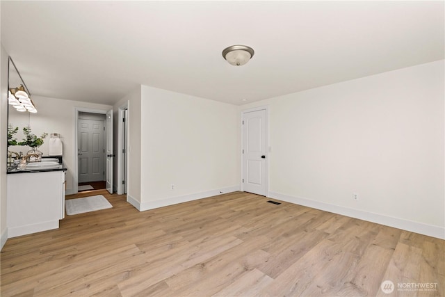 spare room with baseboards, visible vents, a sink, and light wood-type flooring