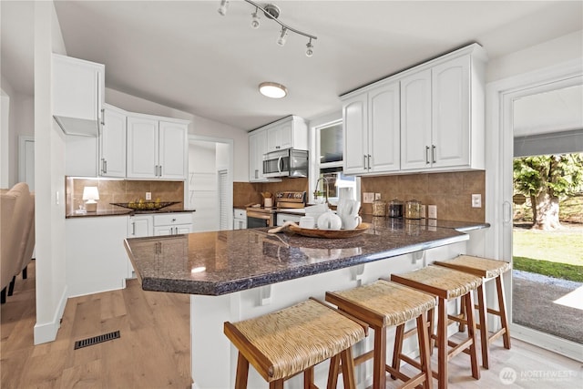 kitchen featuring backsplash, white cabinets, a peninsula, stainless steel appliances, and light wood-style flooring