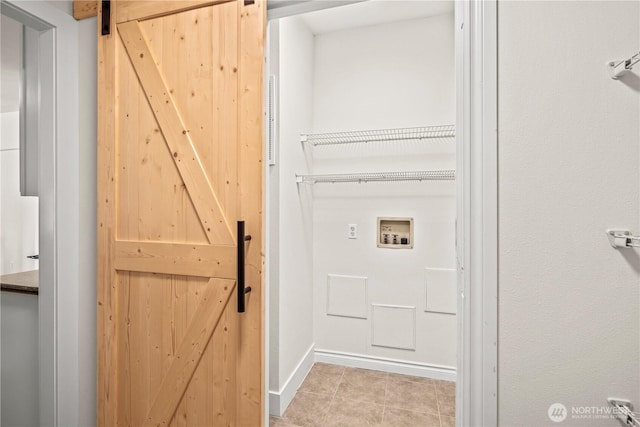 clothes washing area with washer hookup, laundry area, a barn door, tile patterned floors, and baseboards