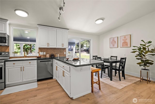 kitchen featuring a peninsula, a breakfast bar area, tasteful backsplash, light wood finished floors, and appliances with stainless steel finishes