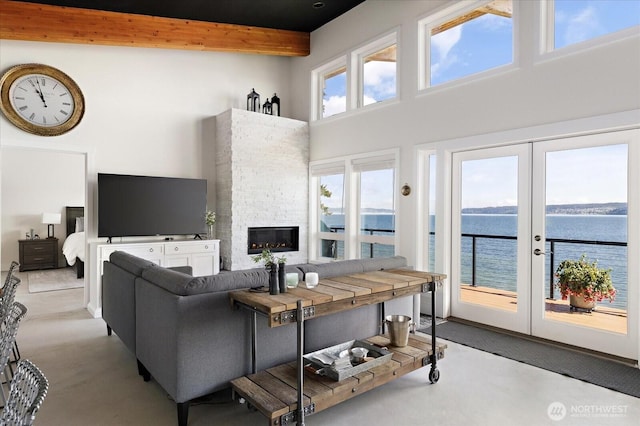 living room featuring french doors, a stone fireplace, finished concrete floors, beam ceiling, and a high ceiling