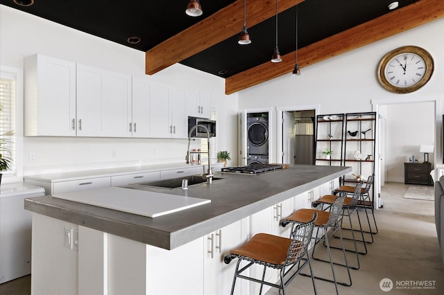 kitchen with beam ceiling, stacked washing maching and dryer, a sink, stainless steel microwave, and white cabinetry