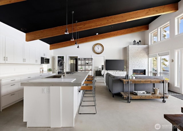 kitchen with beam ceiling, an island with sink, high vaulted ceiling, white cabinetry, and stainless steel microwave