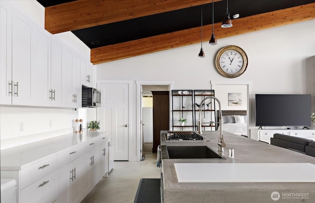 kitchen featuring lofted ceiling with beams, a sink, white cabinetry, open floor plan, and pendant lighting