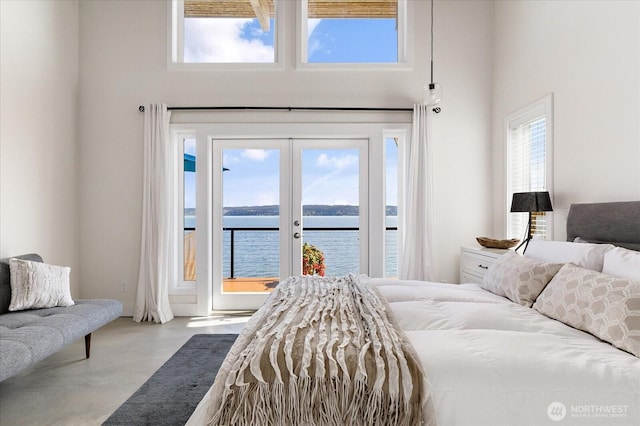 bedroom featuring access to outside, finished concrete flooring, french doors, a towering ceiling, and a water view