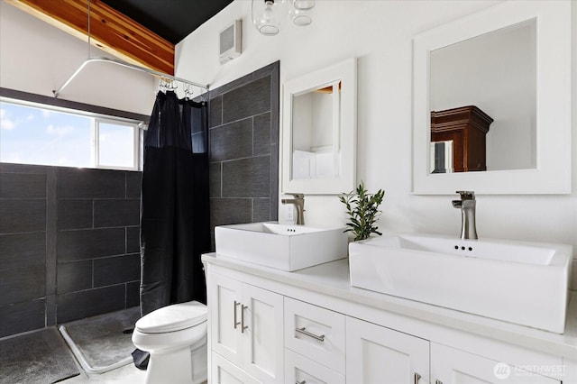 full bath with double vanity, a sink, a tile shower, and toilet