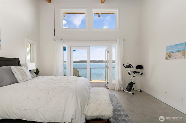 bedroom featuring finished concrete flooring, a water view, a high ceiling, and access to exterior