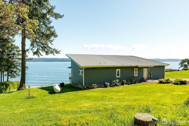 rear view of house with a lawn, a water view, and metal roof