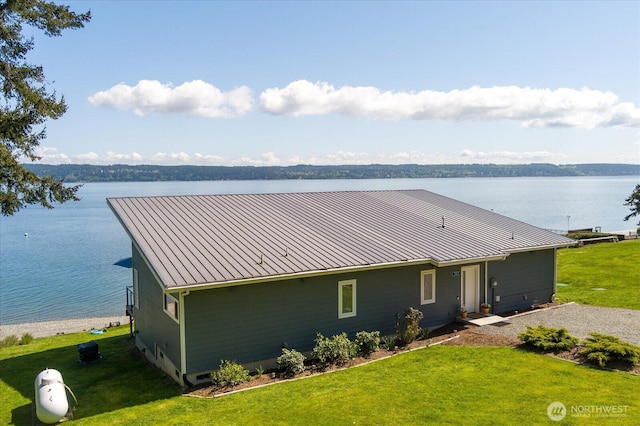 exterior space with a water view, a standing seam roof, a front yard, and metal roof