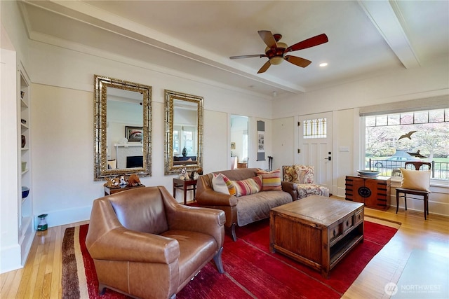 living area with wood finished floors, beam ceiling, ceiling fan, and plenty of natural light