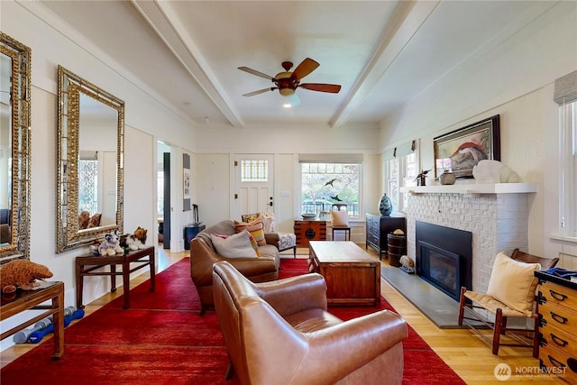 living room featuring a brick fireplace, wood finished floors, beam ceiling, and ceiling fan