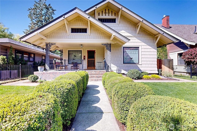 bungalow-style home featuring a chimney, a front lawn, fence, and covered porch