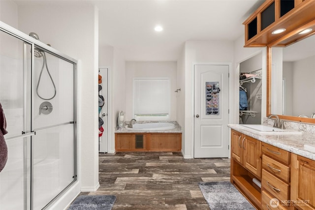 bathroom with vanity, a shower stall, a walk in closet, a garden tub, and wood finished floors