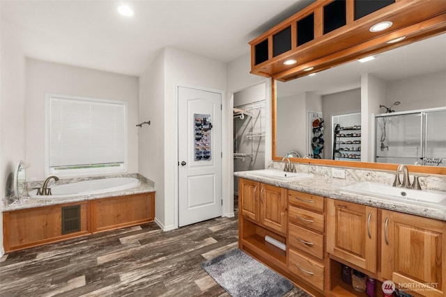 full bath featuring a sink, a spacious closet, a stall shower, and wood finished floors