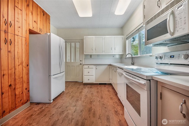 kitchen with white appliances, light wood finished floors, light countertops, a sink, and white cabinets