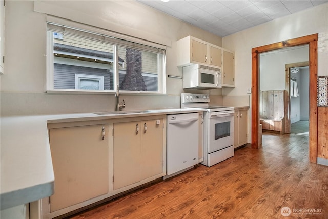 kitchen with white appliances, a sink, wood finished floors, light countertops, and cream cabinets