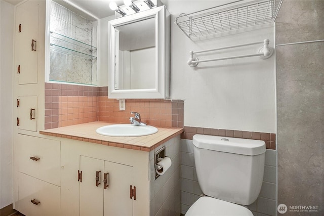half bath with toilet, vanity, wainscoting, and tile walls