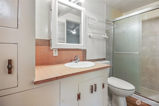 bathroom featuring a stall shower, toilet, vanity, and decorative backsplash