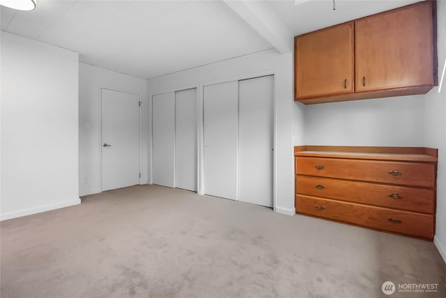 unfurnished bedroom featuring two closets, light colored carpet, and baseboards