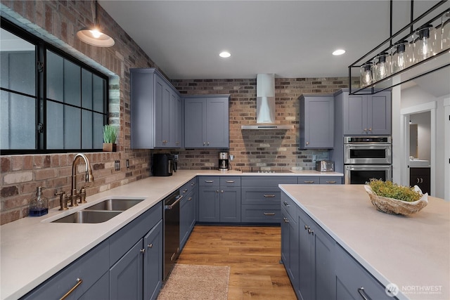 kitchen featuring wall chimney range hood, stainless steel double oven, a sink, dishwasher, and light countertops