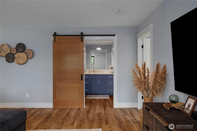 hallway featuring baseboards, a barn door, a sink, and light wood finished floors