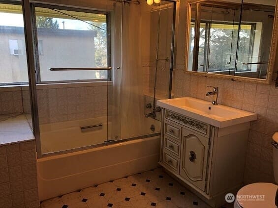 bathroom with a wealth of natural light, enclosed tub / shower combo, tile walls, and toilet