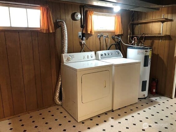 clothes washing area with electric water heater, wood walls, and a healthy amount of sunlight