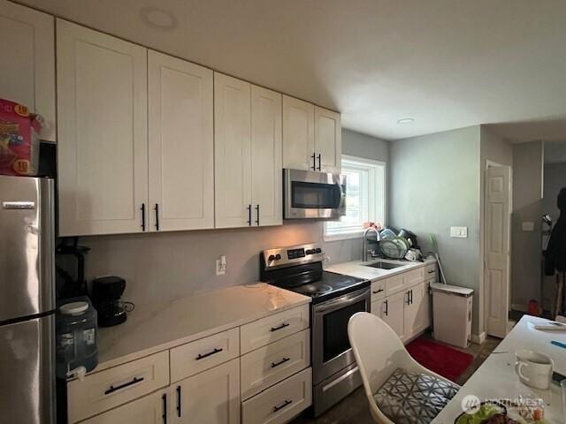kitchen with a sink, light countertops, appliances with stainless steel finishes, and white cabinetry