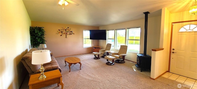 living room with baseboards, a ceiling fan, light colored carpet, and a wood stove