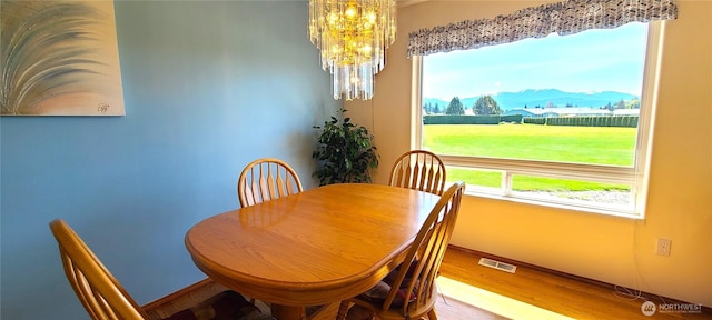 dining room featuring wood finished floors, visible vents, a healthy amount of sunlight, baseboards, and a notable chandelier