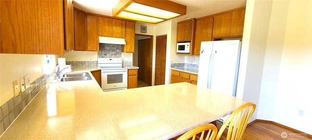 kitchen with a sink, white appliances, light countertops, a peninsula, and under cabinet range hood