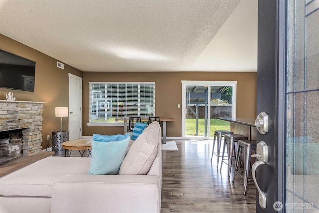 living room featuring a fireplace, a textured ceiling, visible vents, wood finished floors, and baseboards