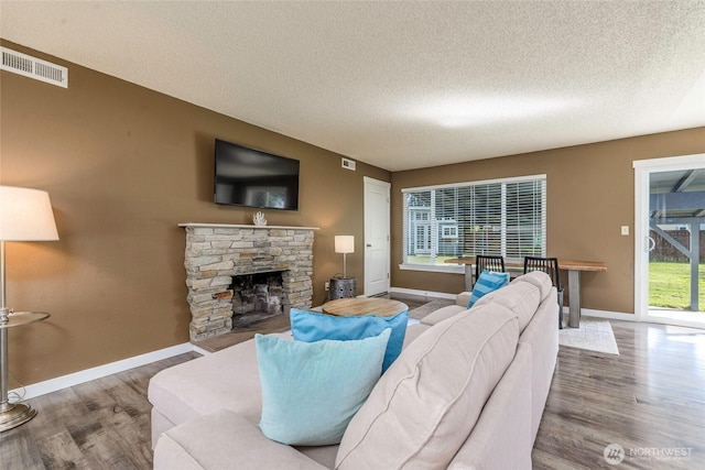 living room with baseboards, a fireplace, a textured ceiling, visible vents, and wood finished floors