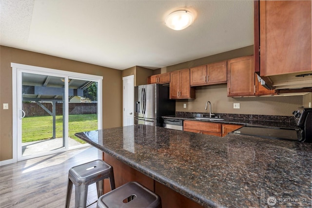 kitchen with a sink, a peninsula, brown cabinetry, wood finished floors, and stainless steel appliances