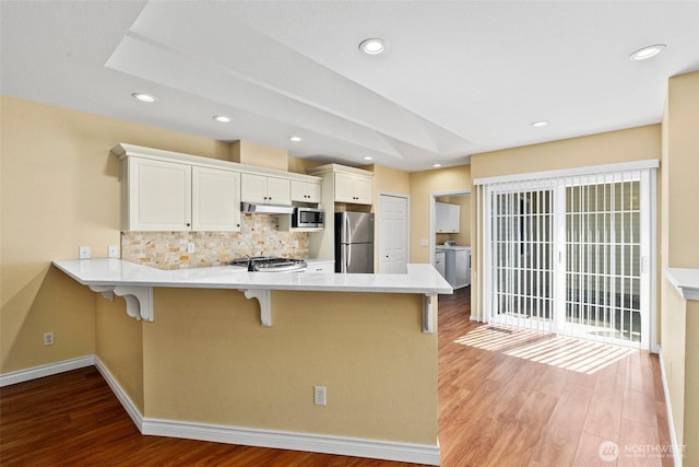 kitchen with a peninsula, a kitchen breakfast bar, tasteful backsplash, light wood-type flooring, and appliances with stainless steel finishes