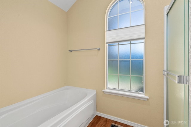 full bath featuring a bath, wood finished floors, baseboards, and a wealth of natural light