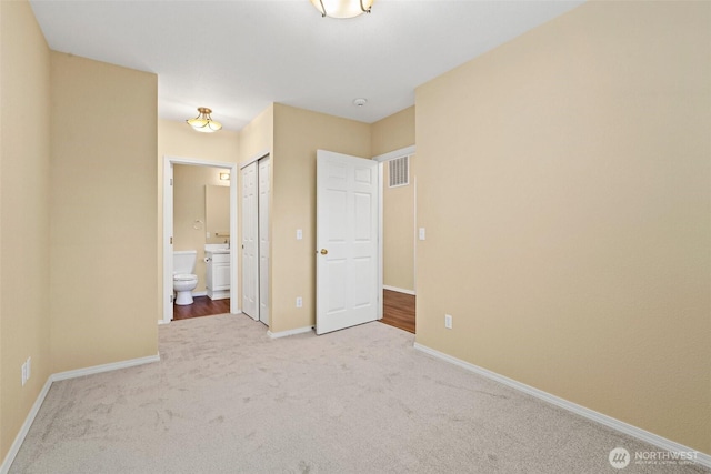 unfurnished bedroom featuring baseboards, ensuite bath, visible vents, and carpet floors