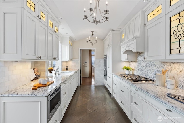 kitchen with an inviting chandelier, dark tile patterned flooring, white cabinets, appliances with stainless steel finishes, and a sink