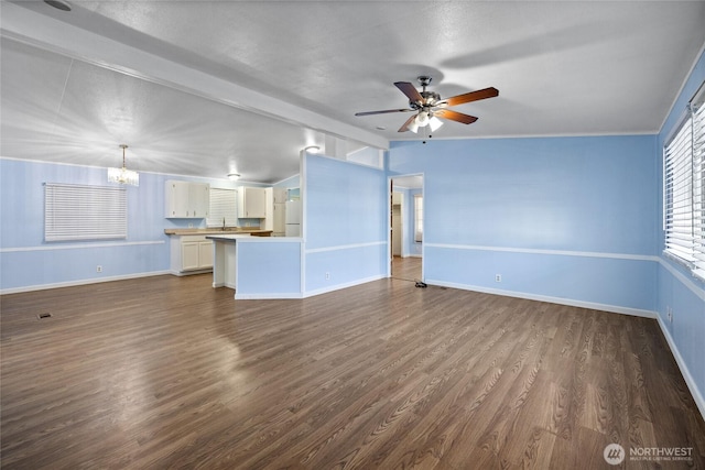 unfurnished living room with dark wood-style floors, ceiling fan with notable chandelier, and baseboards