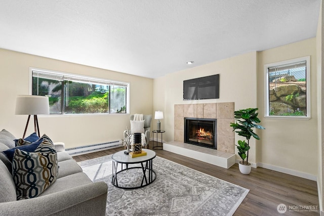 living room with a baseboard radiator, a tile fireplace, plenty of natural light, and wood finished floors