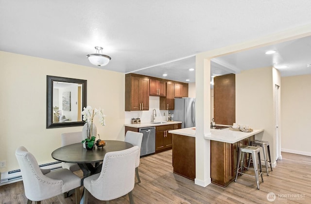kitchen with a sink, a peninsula, a breakfast bar area, light wood-style flooring, and appliances with stainless steel finishes