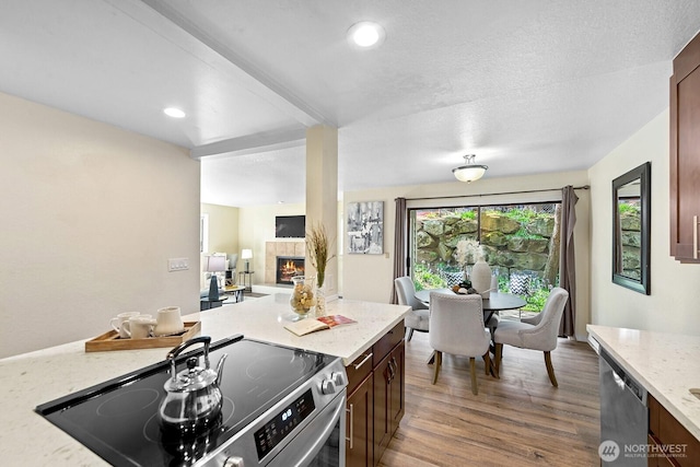 kitchen with a warm lit fireplace, wood finished floors, recessed lighting, light stone countertops, and appliances with stainless steel finishes