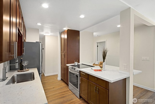 kitchen featuring light wood finished floors, a sink, stainless steel range with electric cooktop, baseboards, and light stone counters