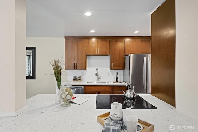 kitchen featuring a sink, stainless steel appliances, brown cabinets, recessed lighting, and light stone countertops