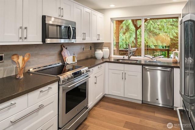 11820 NE 145th St, Kirkland, WA 98034 - kitchen featuring white cabinets, light wood finished floors, dark countertops, a sink, and appliances with stainless steel finishes