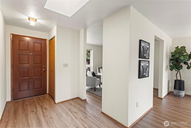 entryway featuring light wood-type flooring, baseboards, and a skylight