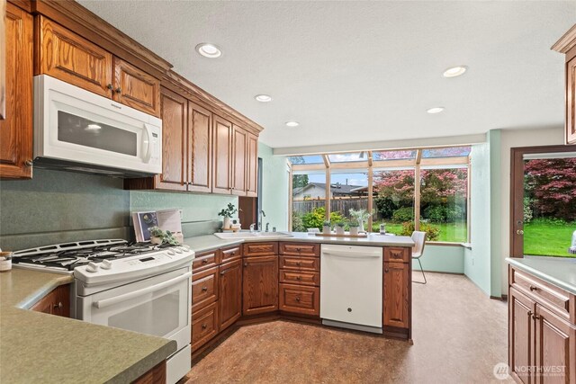 kitchen with brown cabinetry, a sink, light countertops, recessed lighting, and white appliances